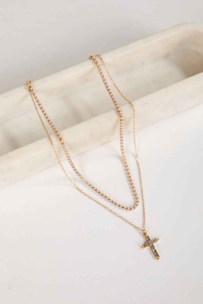 Two gold necklaces with a cross pendant on a white surface