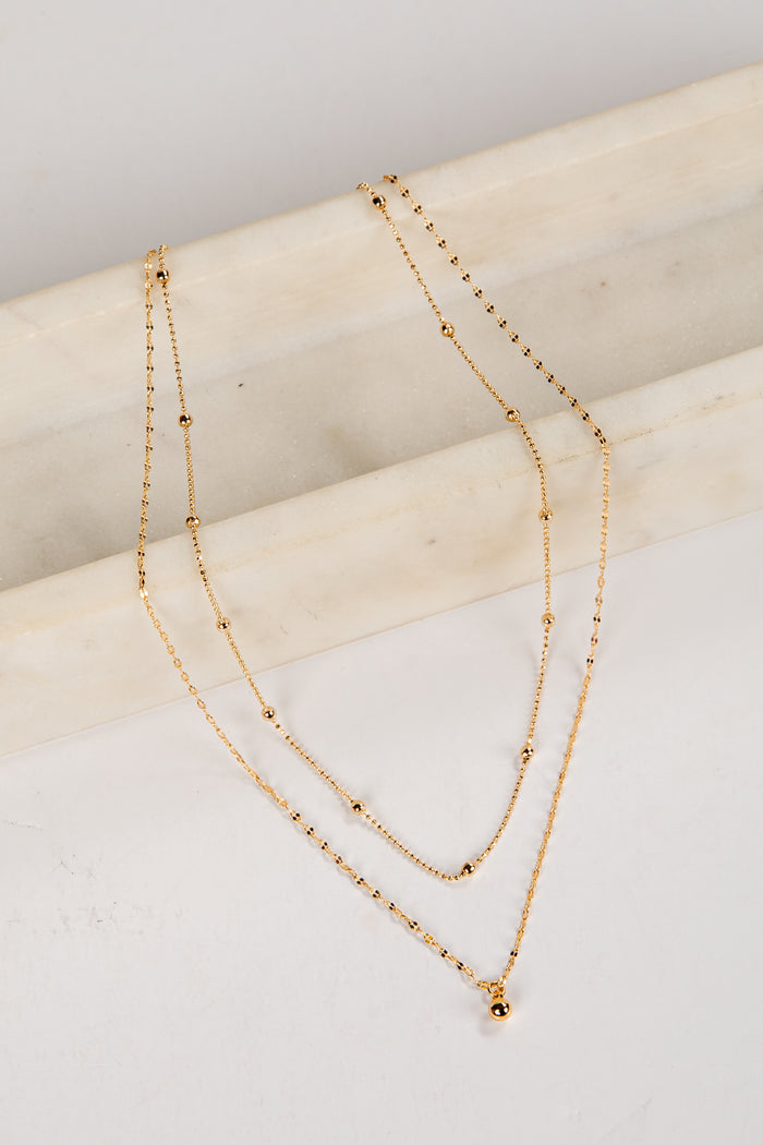 Two gold necklaces on a light wooden surface