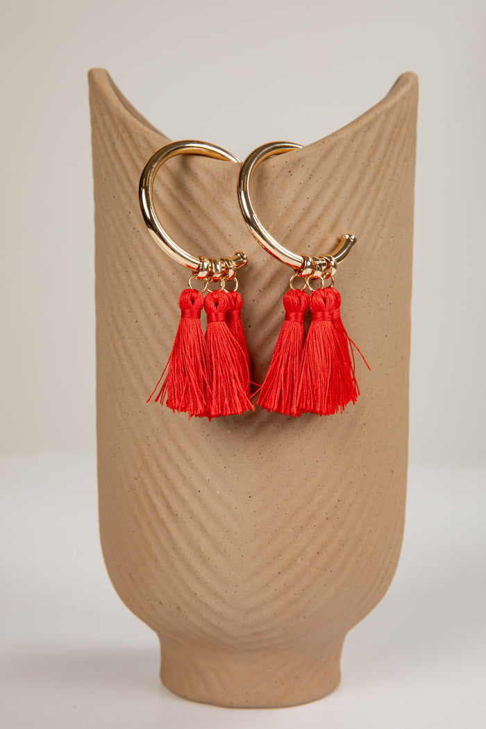 Gold hoop earrings with red tassels on a beige stand.