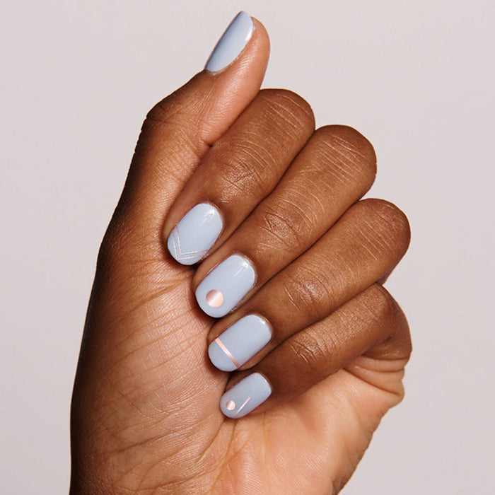 Hand with nails in pale blue polish featuring On the Dotted Line geometric mani with white and rose gold lines and dots
