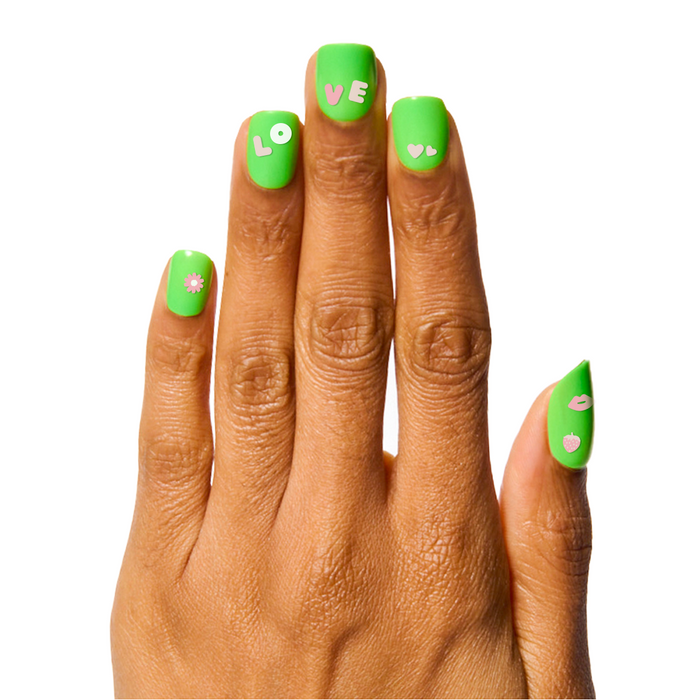 Hand with bright green polish and pink Pink Letters nail art stickers spelling LOVE with hearts and icons for manicures