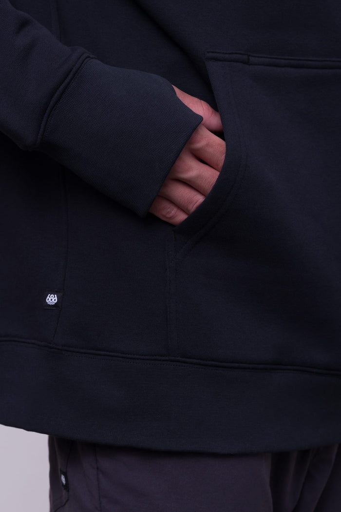A person wearing the 686 Mens Knockout Pullover Hoody has one hand inside its front pocket. Only the torso and hand are visible.