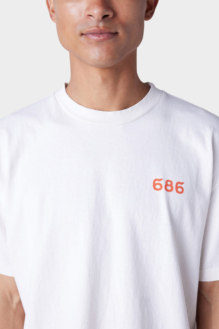A person wearing the 686 Mens Man in the Sun Short Sleeve Tee by 686, a white crew-neck t-shirt featuring 686 in small red text on the left chest. Photo focuses on upper torso and shirt, cropped just below the nose.
