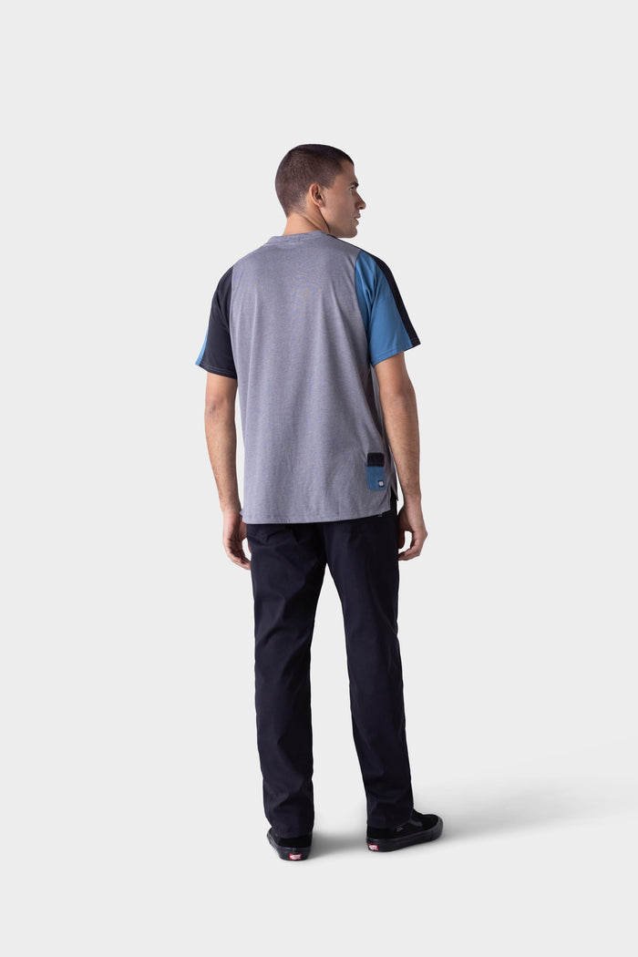A man faces away in a loose gray tee with blue and black sleeves, paired with black 686 Mens Platform Bike Pant - Relaxed Fit by 686, and black shoes, set against a plain light background.