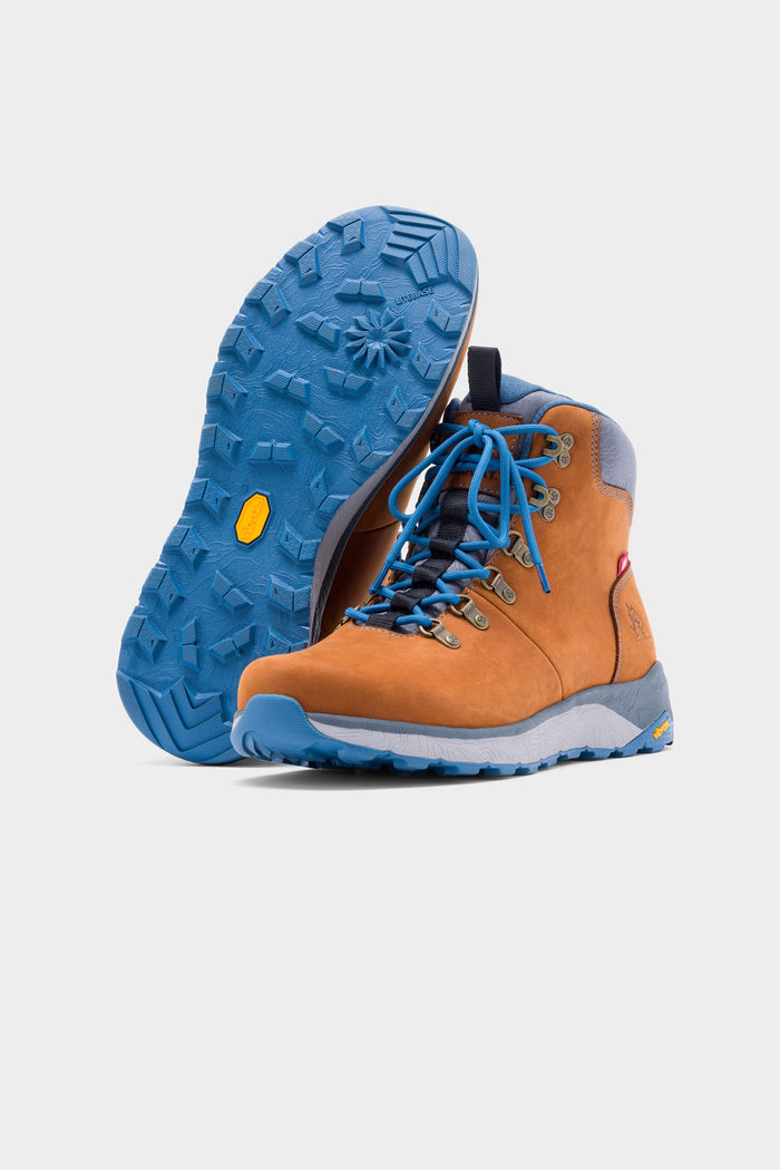 The 686 x Rocky Boots Mens Summit Elite Boot features tan uppers with blue soles and laces; one boot stands upright while the other displays its rugged blue sole, both set against a plain white background.