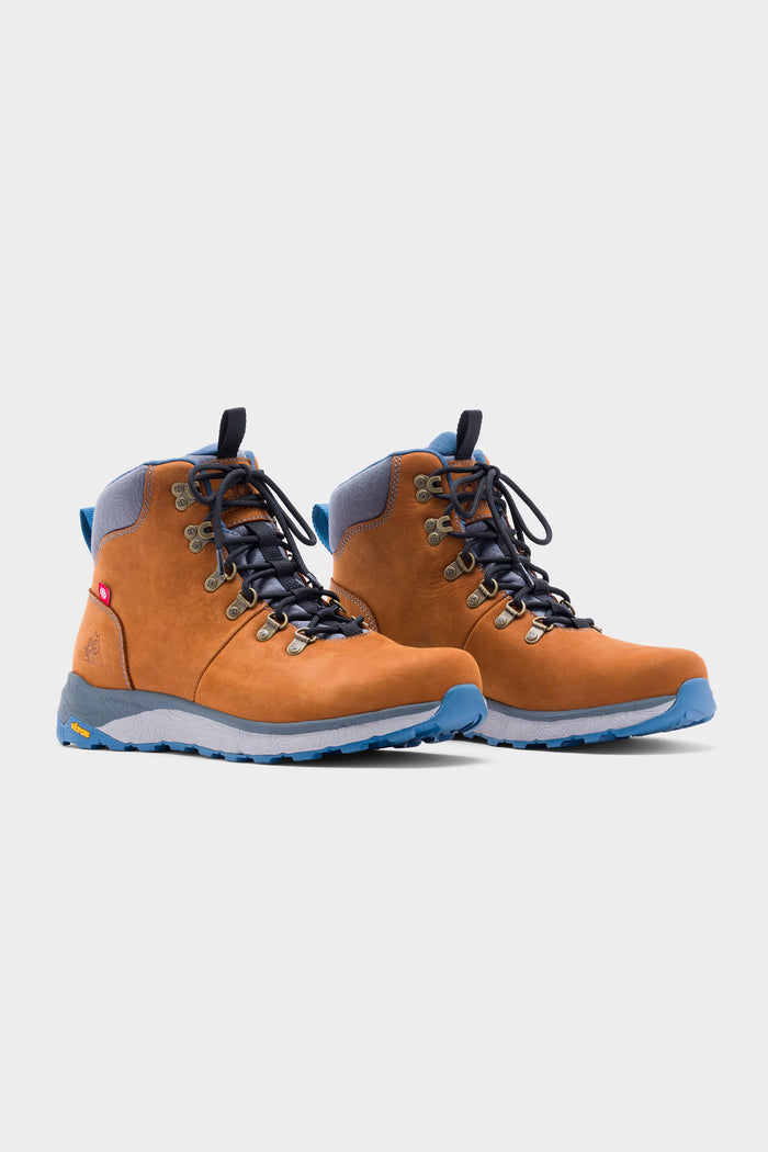 The 686 x Rocky Boots Mens Summit Elite Boot, featuring tan and blue colors, black laces, and rugged blue soles, is displayed against a plain white background.