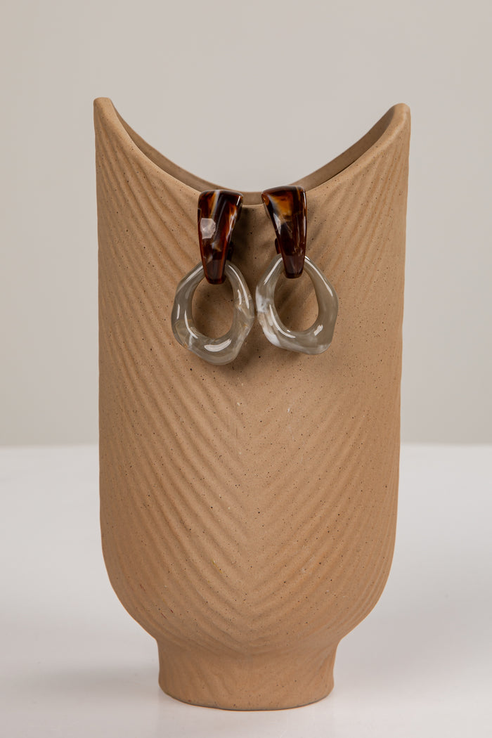 Pair of earrings on a textured brown stand against a plain background