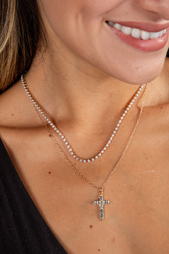 Close-up of a woman wearing a gold necklace with a cross pendant.