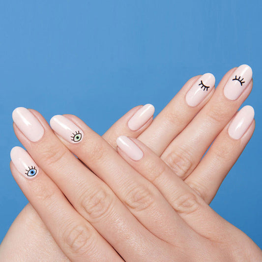 Hands with All Eyes On You manicure featuring nude polish and playful eye designs on nails against a blue background