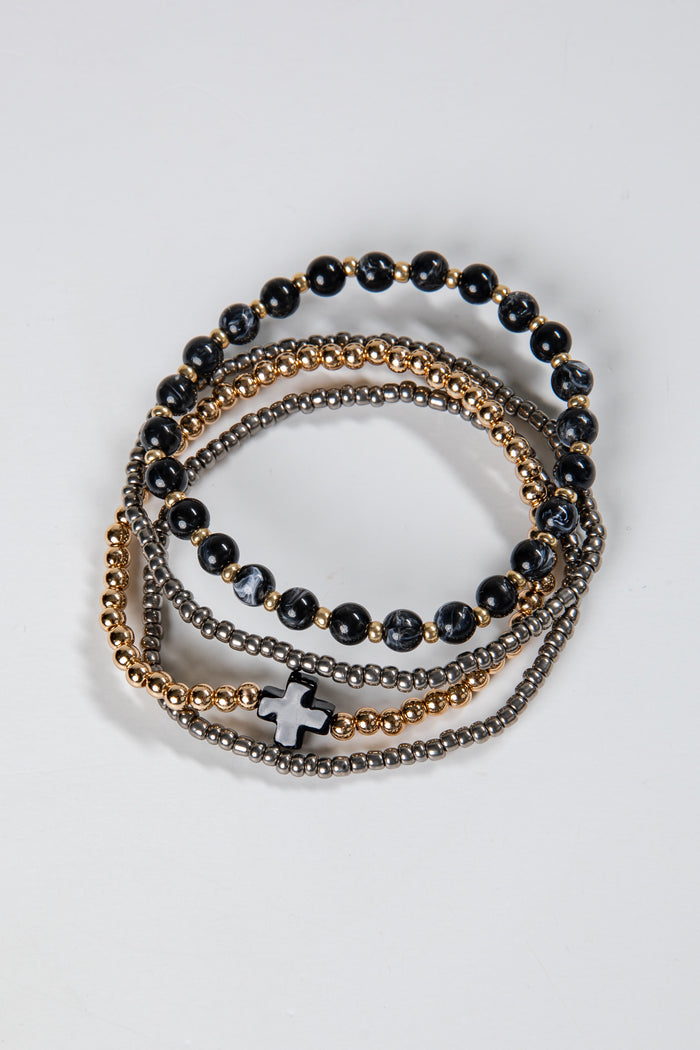 Stack of black beaded bracelets with gold and silver accents on a light gray background