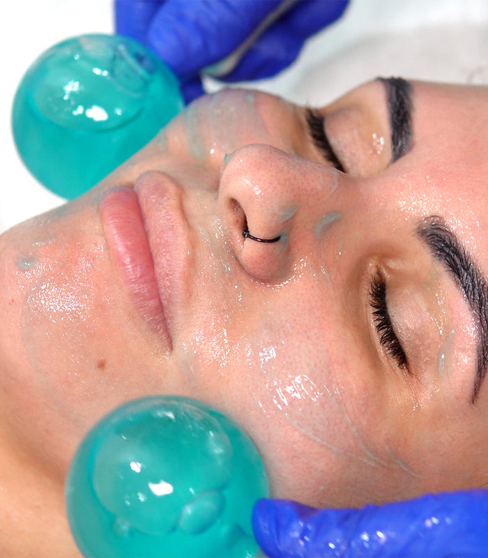 A close-up image of a person receiving a facial treatment with blue gel on their face and teal-colored globes applying the product.
