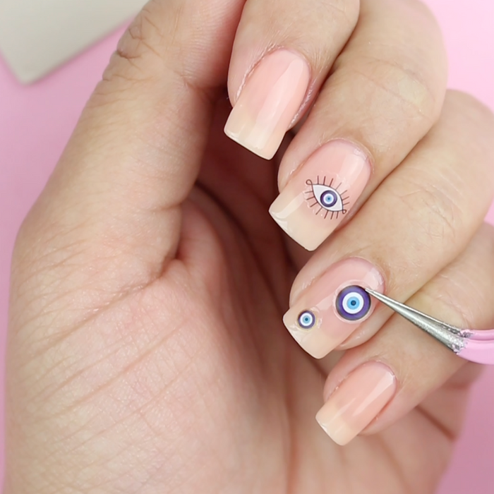 Applying Karma evil eye decals to a sheer pink nail with the tweezer