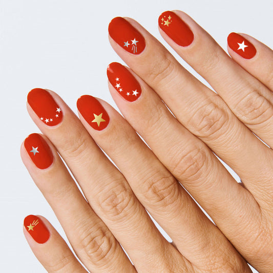 Hand with nails in red polish featuring Lucky Stars metallic gold, silver, and white star-shaped nail art stickers