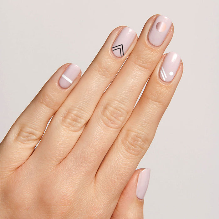 Hand with nails featuring On the Dotted Line manicure with geometric lines and dots in white and black on pale pink polish