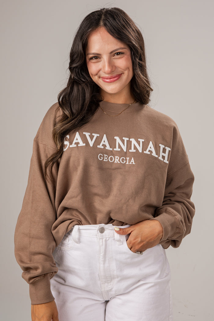 Woman wearing a brown sweatshirt with 'Savannah, Georgia' text against a plain background