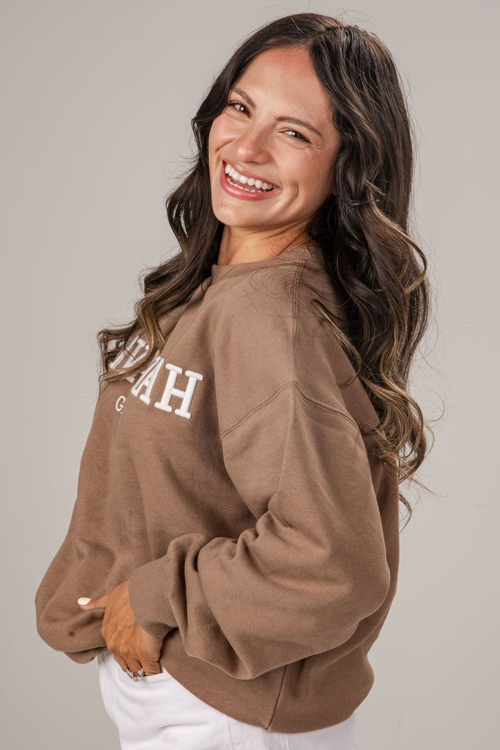 Woman wearing a brown sweatshirt with 'Idaho' printed on it, smiling against a plain background