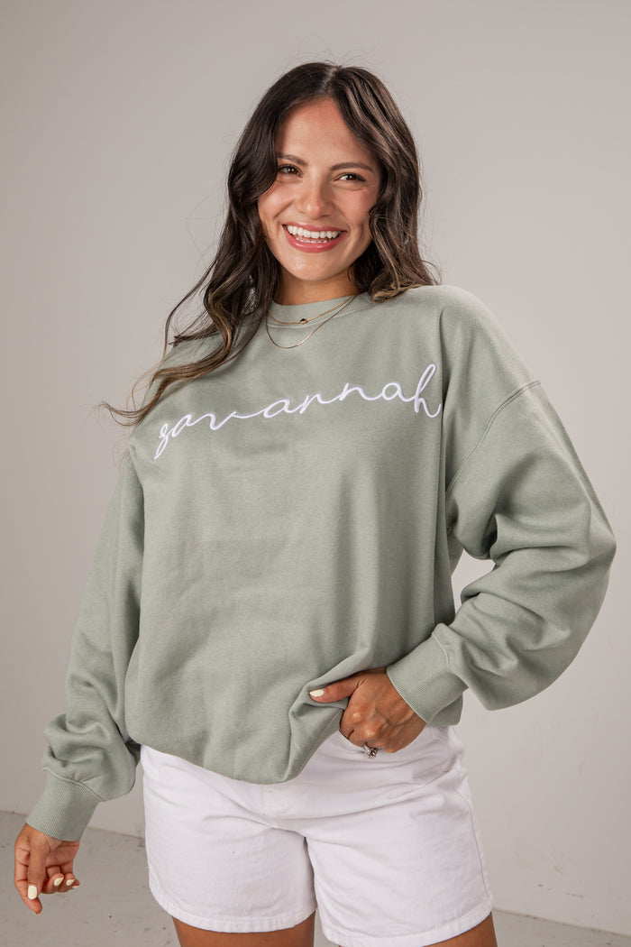 Woman wearing a green sweatshirt with 'Savannah' printed on it, standing against a plain background.