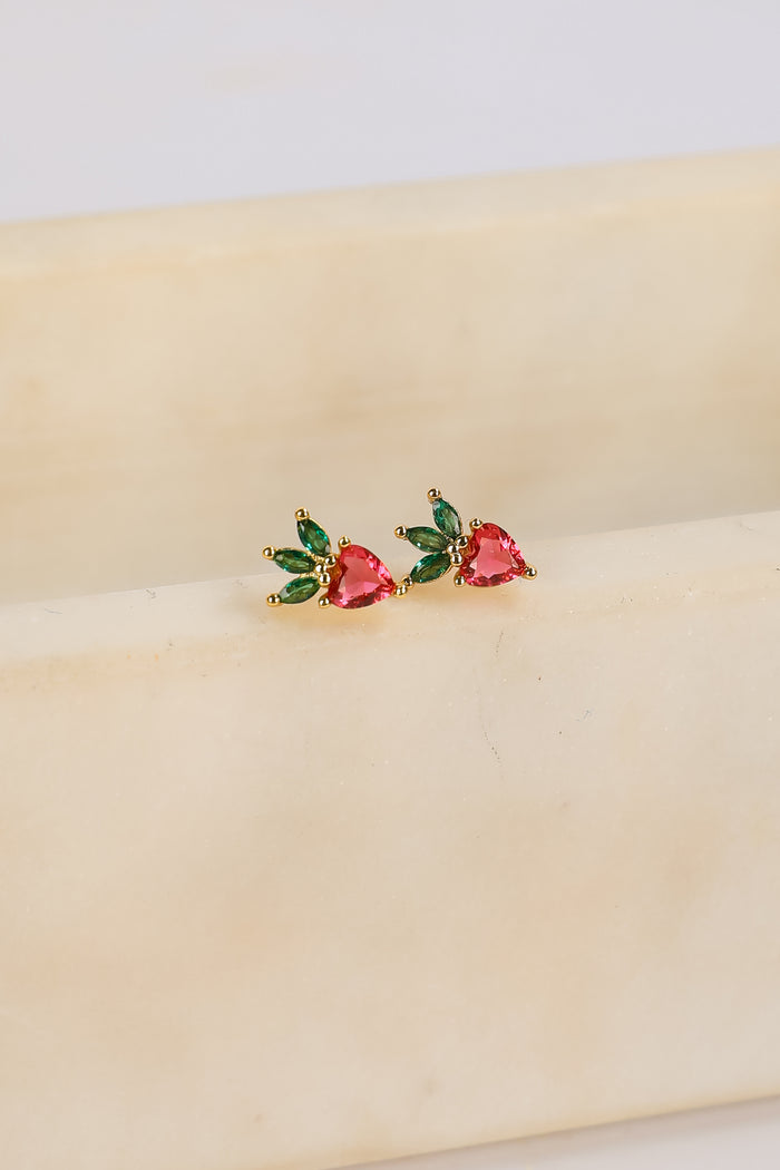 Heart-shaped earrings with green and red stones on a beige surface