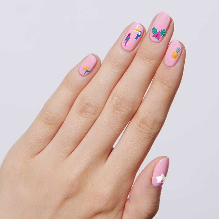 Hand with pink polish featuring Tropical Vibes nail art including toucans, hibiscus, and tropical leaves for mani decor
