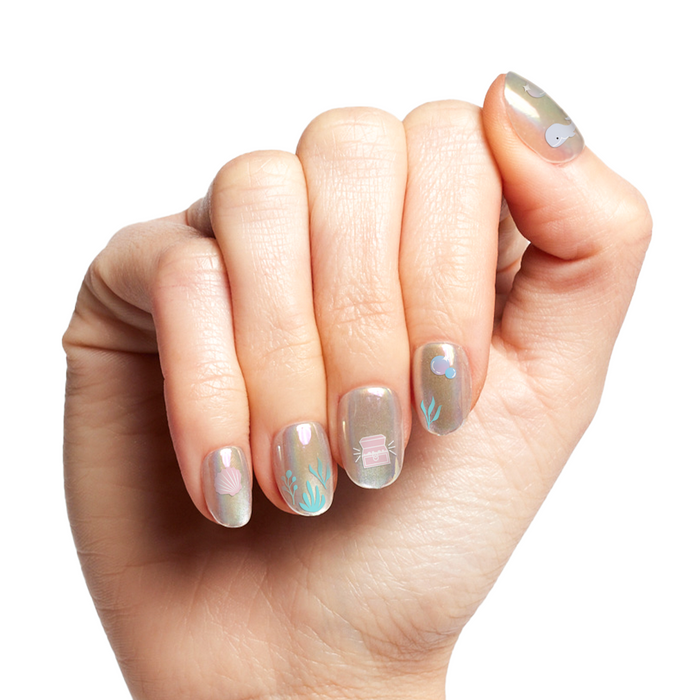 Hand with shimmer polish and Under the Sea nail art stickers featuring seaweed, shells, and underwater designs for manicures
