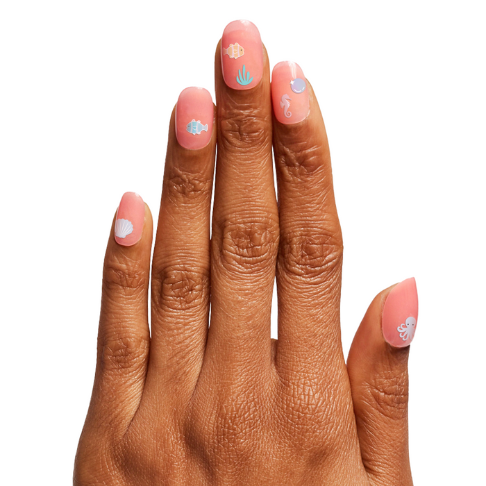 Hand with soft pink gel polish and Under the Sea nail stickers showcasing sea creatures and shells for at home manicures